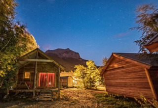 Chalets en bois éclairés la nuit à Huttopia Vallouise, Provence-Alpes-Côte d’Azur, sous un ciel étoilé.