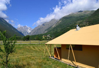 Una tienda en un campo verde rodeado de montañas y cielo azul en Huttopia Vallouise, Provenza-Alpes-Costa Azul, Francia.
