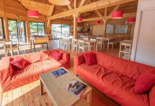 Salon spacieux à Huttopia Vallouise avec canapés rouges, intérieur en bois et grandes baies vitrées donnant dehors.