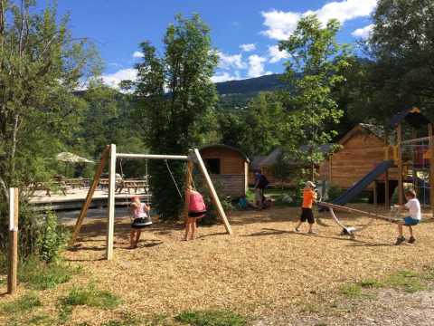 Niños jugando en columpios y balancín en un parque infantil de Huttopia Vallouise, Francia.