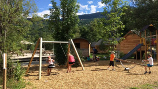 Niños jugando en columpios y balancín en un parque infantil de Huttopia Vallouise, Francia.