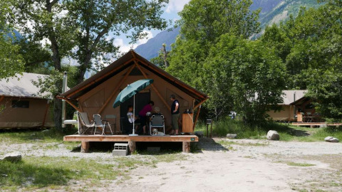 Familia relajándose en la terraza de una cabaña en Huttopia Vallouise, rodeada de naturaleza y montañas.