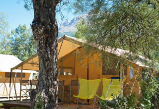 Glamping telt med gule stole på en træveranda, omgivet af natur ved Huttopia Vallouise, Provence-Alpes-Côte d’Azur.