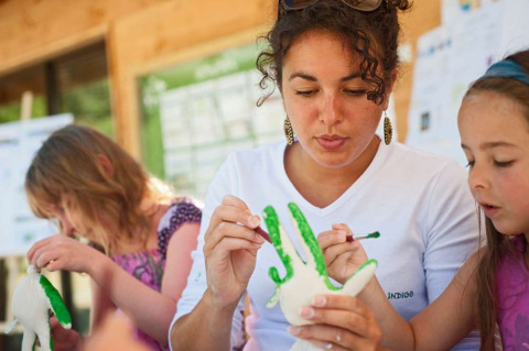 Una mujer y niños pintan figuras de arcilla al aire libre en el parque vacacional Huttopia Vallouise, Francia.
