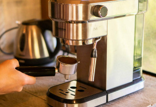 Una máquina de café espresso en uso en una tienda safari en Camping Les 3 Cantons, Francia, con tetera al fondo.