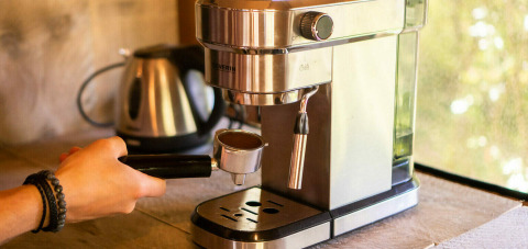Una máquina de café espresso en uso en una tienda safari en Camping Les 3 Cantons, Francia, con tetera al fondo.