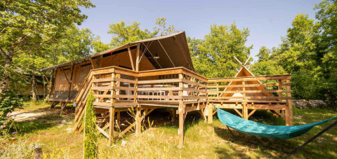 Safari Lodge e Teeny Lodge su una piattaforma di legno, con amaca e alberi verdi sotto il sole.