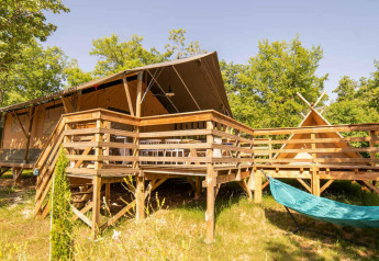 Safari Lodge et Teeny Lodge sur une terrasse en bois avec hamac, entourées d’arbres verts et de soleil.