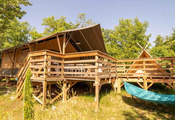 Tienda Safari Lodge y Teeny Lodge sobre una plataforma de madera, hamaca y árboles verdes bajo el sol.
