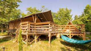 Tienda Safari Lodge y Teeny Lodge sobre una plataforma de madera, hamaca y árboles verdes bajo el sol.