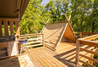 Houten terras met keukentje en klein tentje bij Safari Lodge, Camping Les 3 Cantons, Frankrijk, tussen de bomen.