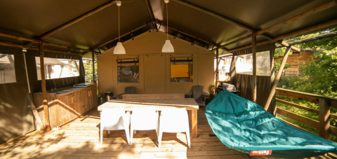 Safari Lodge + Teeny Lodge: terraza de madera con mesa, silla hamaca y cocina exterior en Camping Les 3 Cantons.