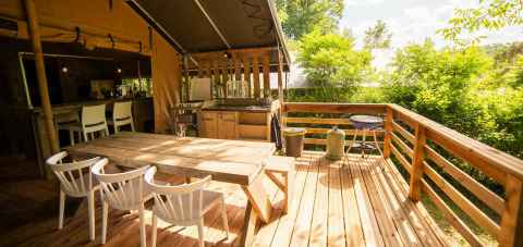 Terraza exterior de la tienda Safari Lodge en Camping Les 3 Cantons, Francia, con cocina y comedor de madera.