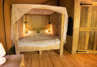 Vista interior de la tienda Safari Lodge en Camping Les 3 Cantons, Francia, con cama dosel y decoración de madera.