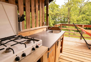 Outdoor kitchen with gas stove, sink, and hammock on wooden deck at Safari Lodge, Camping Centro Vacanze San Marino.