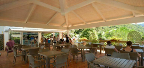 Zona pranzo esterna al Camping Delle Rose in Liguria, Italia, con ospiti e vista sul verde.