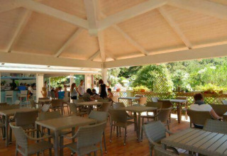 Outdoor dining area at Camping Delle Rose in Liguria, Italy, with guests and a view of greenery.