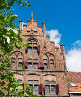 Historisk bygning af mursten under blå himmel med grønne blade foran, set i en feriepark med glamping.