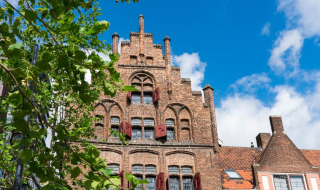 Edificio histórico de ladrillo con contraventanas rojas y cielo azul, visto en un parque de vacaciones glamping.