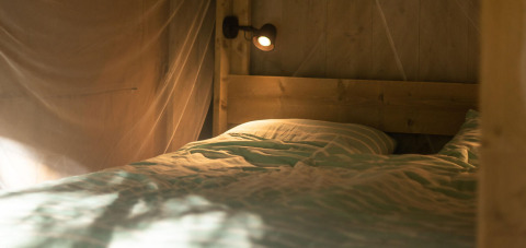 Cama acogedora con sábanas de rayas en tienda Safari lodge en Camping Delle Rose, Italia, luz suave.