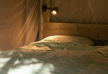 Cama acogedora con sábanas de rayas en tienda Safari lodge en Camping Delle Rose, Italia, luz suave.
