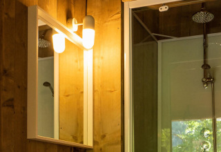 Bathroom inside Safari lodge tent at Camping Delle Rose, featuring a lit mirror and a modern shower.