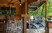 Interno tenda safari lodge al Camping Delle Rose, Italia, con sgabelli da bar, veranda e vista sugli alberi.