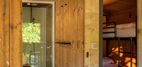 Interior de una tienda Safari lodge en Camping Delle Rose, Italia, con literas y baño moderno visibles.
