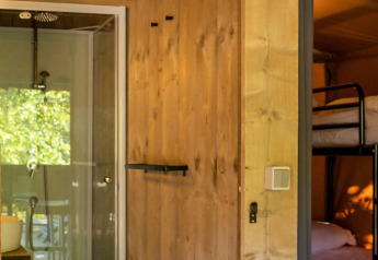 Interior de una tienda Safari lodge en Camping Delle Rose, Italia, con literas y baño moderno visibles.