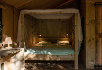 Interior de una tienda Safari Lodge en Camping Delle Rose, Italia, con cama doble y decoración de madera.