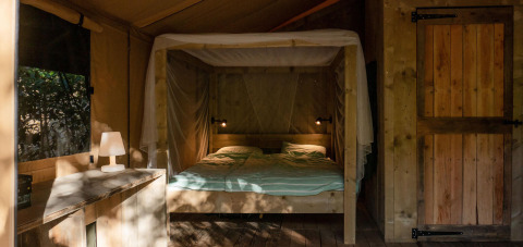 Binnenkant van een Safari Lodge tent op Camping Delle Rose in Italië met tweepersoonsbed en houten meubels.