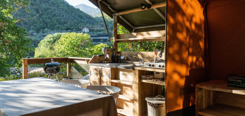Cocina exterior de una tienda safari en Camping Delle Rose, Italia, con vistas a montañas verdes.