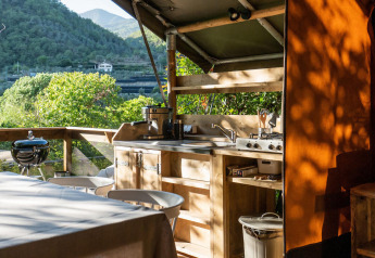 Cocina exterior de una tienda safari en Camping Delle Rose, Italia, con vistas a montañas verdes.