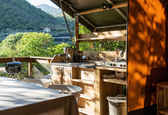 Buitenkeuken van een safaritent op Camping Delle Rose in Italië, uitkijkend over het groene berglandschap.