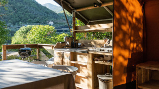 Cocina exterior de una tienda safari en Camping Delle Rose, Italia, con vistas a montañas verdes.
