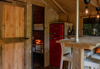 Interior de la tienda Safari Lodge en Camping Delle Rose, Italia, con muebles de madera y nevera roja.