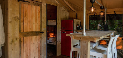 Indretning af Safari Lodge-telt på Camping Delle Rose i Italien, med træmøbler og rød retro-køleskab.