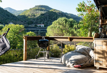 Terraza de madera en Safari Lodge con hamaca, puff, barbacoa y cocina exterior con vistas a colinas verdes.