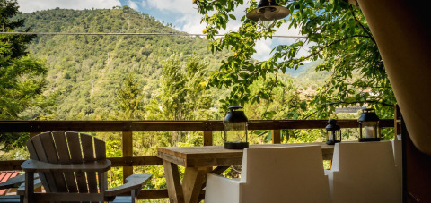 Vista desde la tienda safari Base Lodge en Camping Delle Rose, Italia, con sillas, mesa y paisaje montañoso.