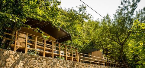 Safari-Zelt namens Base Lodge auf einer Steinmauer, umgeben von üppigem grünen Wald und Bäumen.