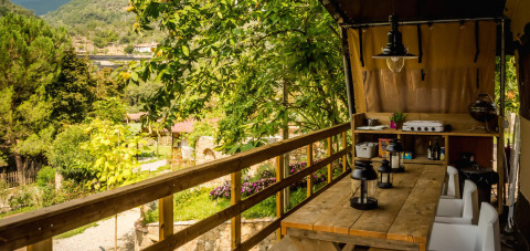 Terraza de madera en tienda safari Base Lodge en Camping Delle Rose, Italia, con vistas y zona de comedor.