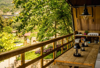 Terraza de madera en tienda safari Base Lodge en Camping Delle Rose, Italia, con vistas y zona de comedor.