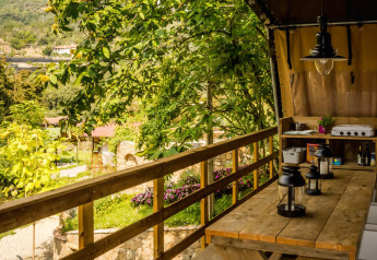 Wooden deck of Base Lodge safari tent at Camping Delle Rose, Italy, featuring outdoor dining and greenery.