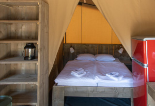 Interior de la tienda safari Base Lodge en Camping Delle Rose, Italia, con cama doble y nevera roja visible.