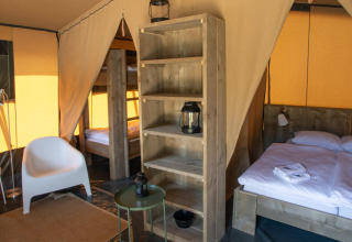 Interior de tienda safari Base Lodge en Camping Delle Rose, Italia, con cama, sillas y estantería.
