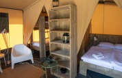 Interior of Base Lodge safari tent at Camping Delle Rose, Italy, showing bed, chairs, and shelving unit.
