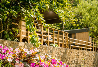 Blumenbeet vor dem Safari-Zelt Base Lodge im Camping Delle Rose, Italien, umgeben von Bäumen und Natur.