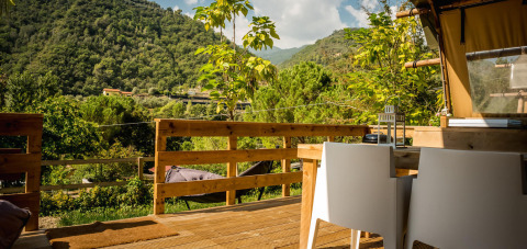 View from a Desert Lodge safari tent at Camping Delle Rose, Italy, with wooden deck and lush mountain scenery.