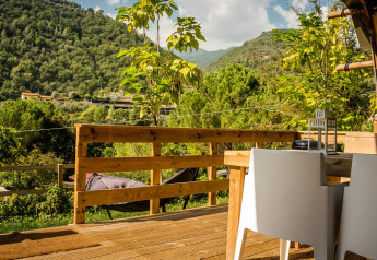 View from a Desert Lodge safari tent at Camping Delle Rose, Italy, with wooden deck and lush mountain scenery.