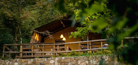 Tienda safari Desert Lodge en Camping Delle Rose, Italia, rodeada de vegetación y una terraza de madera.